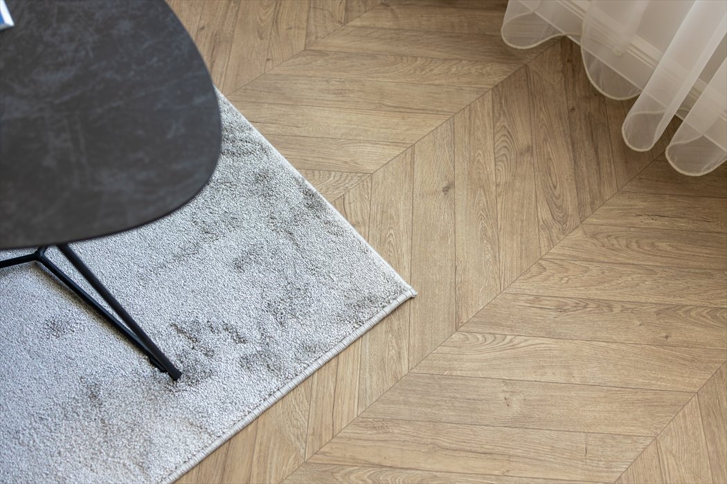 A dark table beside a pale rug, wood floor, and sheer curtains.