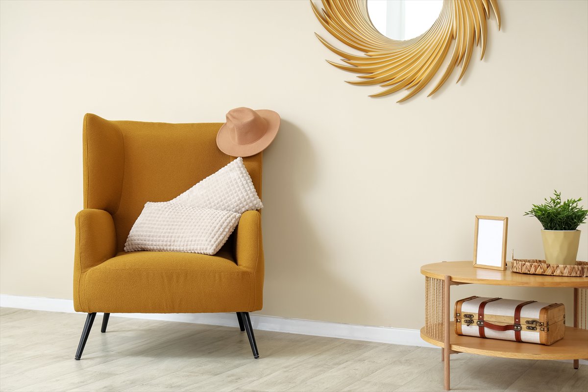 A mustard armchair with a hat and white cushion.