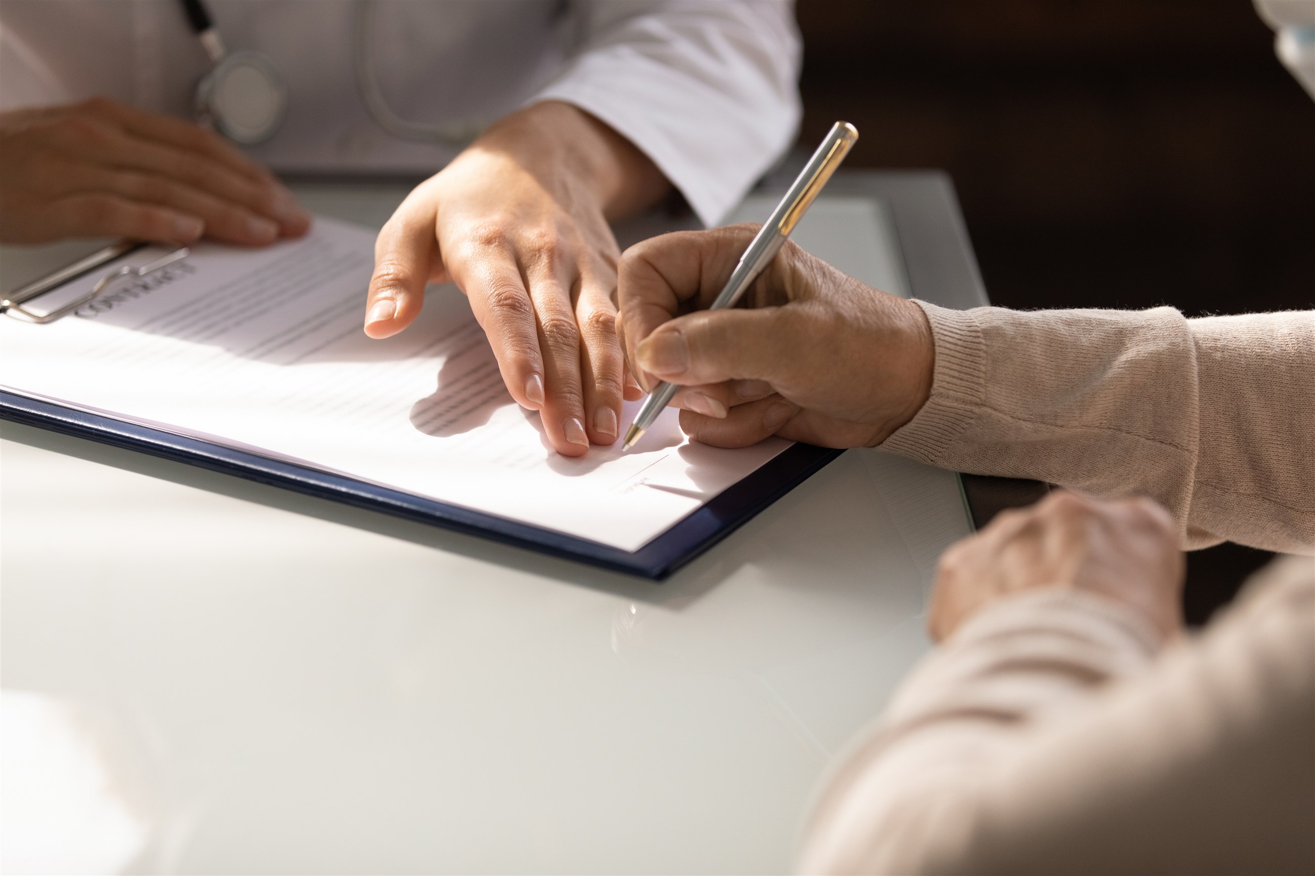 Two people's hands over a document on a clipboard; one holds a pen.